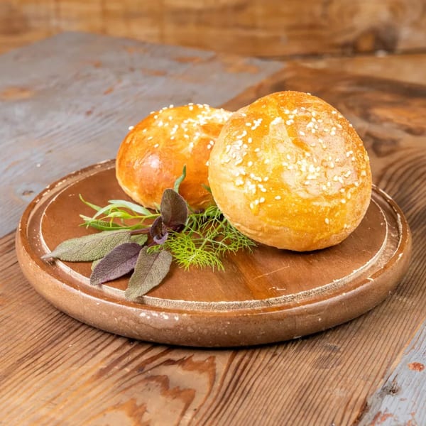 Two golden sesame seed buns with fresh herbs on a rustic wooden board.