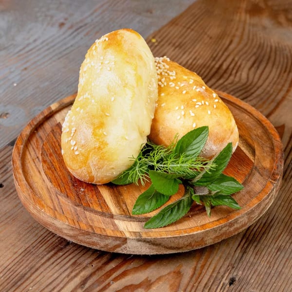 Two golden-brown pastries with sesame seeds and fresh herbs on a wooden serving board.