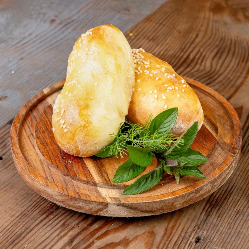 Two golden-brown pastries with sesame seeds and fresh herbs on a wooden serving board.