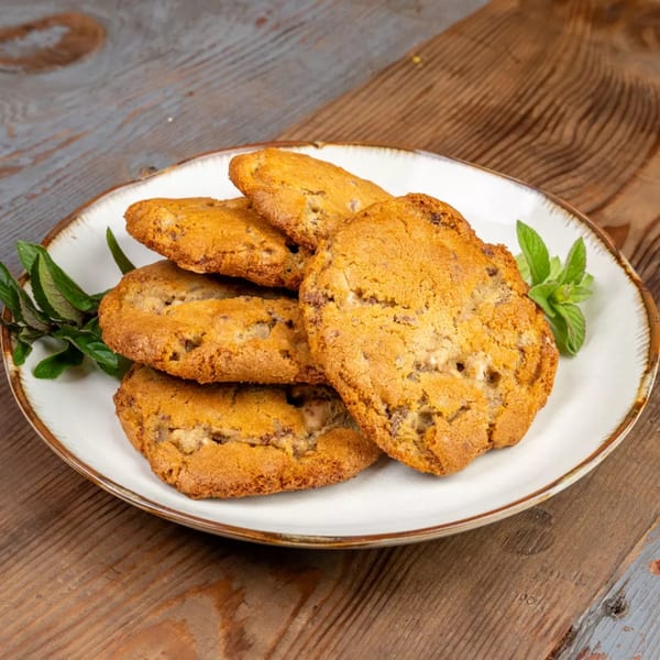 A white plate with a brown rim holds several golden-brown cookies and fresh mint sprigs.