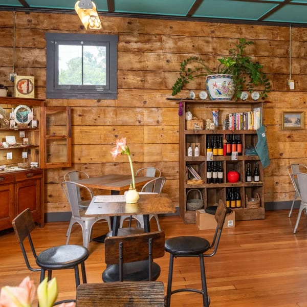 Cozy restaurant interior with wooden walls, tables, chairs, and shelves filled with bottles and books.