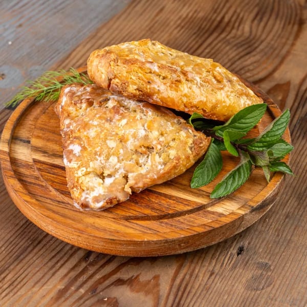 Two golden-brown pastries with white icing and fresh mint leaves on a round wooden board.