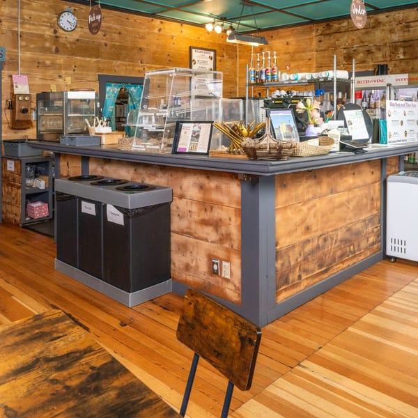 A rustic cafe interior with a wooden counter, display cases, and a "Pick Up Here" sign.