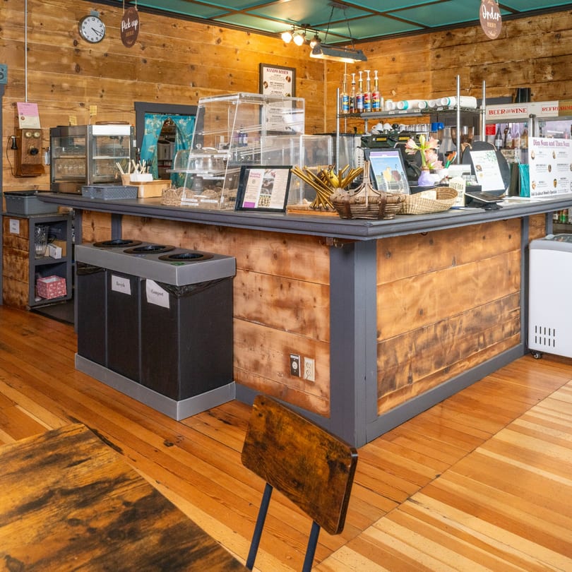 A rustic cafe interior with a wooden counter, display cases, and a "Pick Up Here" sign.