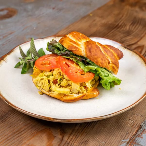 Chicken salad sandwich on a croissant with lettuce and tomato, garnished with herbs on a plate.