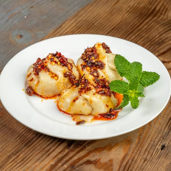 Three dumplings topped with chili oil and fresh mint on a white plate.