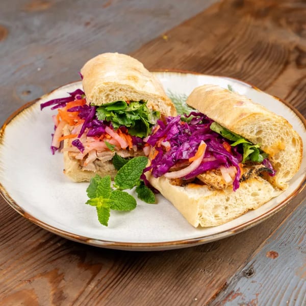 Two vibrant banh mi sandwiches with purple cabbage, carrots, and fresh mint on a white plate.