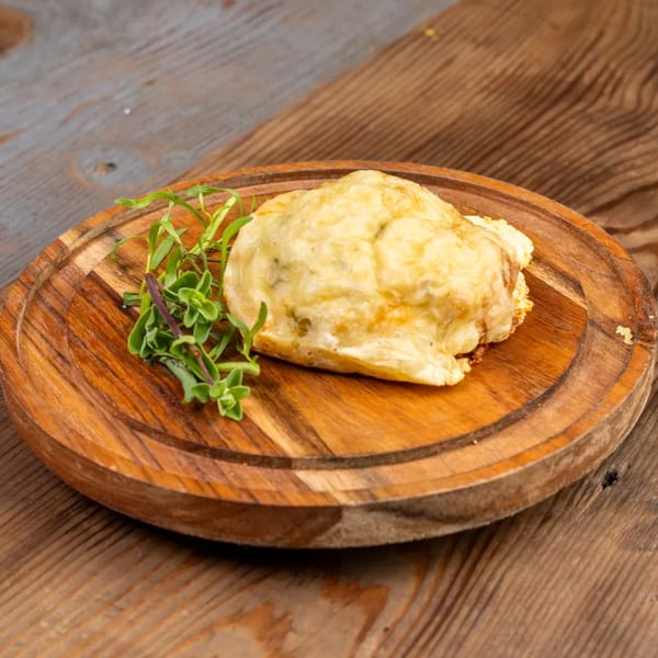 Golden-brown baked dish with melted cheese and fresh herbs on a rustic wooden board.