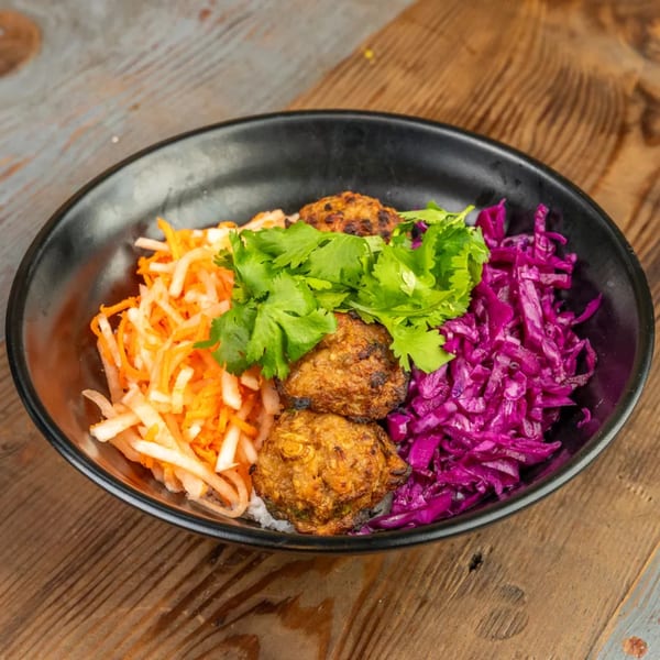 A black bowl filled with rice, three meatballs, shredded carrots, purple cabbage, and fresh cilantro.