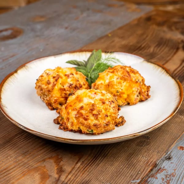 Three golden-brown fried cheese balls garnished with fresh herbs on a white plate.